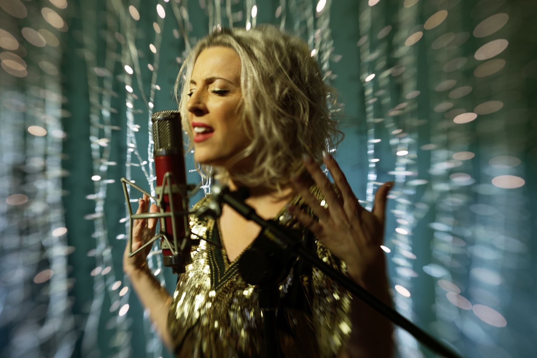 Mia Praught singing into a vintage microphone in a gold dress